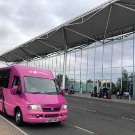 The pink party bus being used for a airport transfer